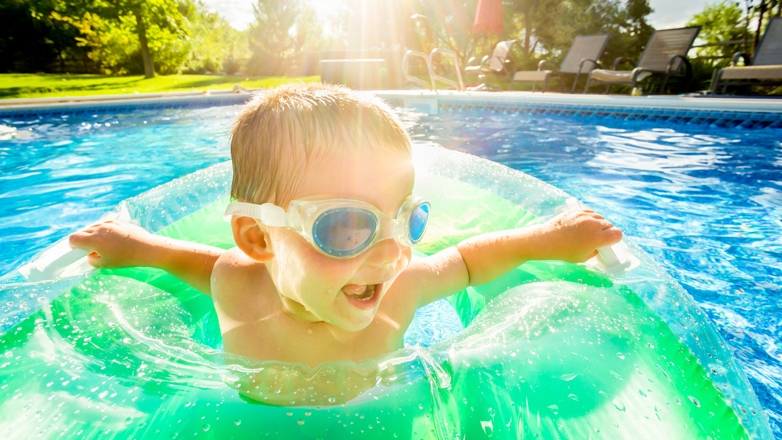 Small child wearing swimming goggles with a round floatie in a residential backyard pool.